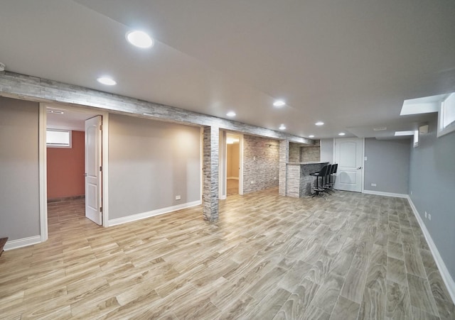 basement with brick wall, indoor bar, and light wood-type flooring