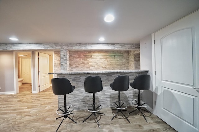 kitchen with light stone counters, a kitchen bar, kitchen peninsula, and light wood-type flooring