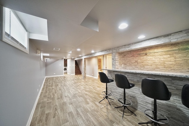 bar with light stone counters and light hardwood / wood-style floors