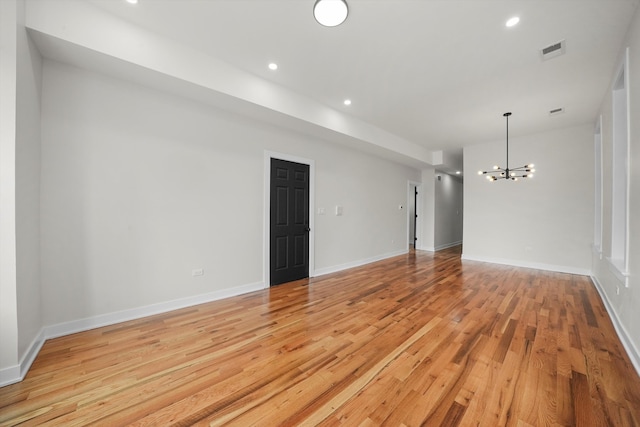 empty room featuring an inviting chandelier and light hardwood / wood-style flooring