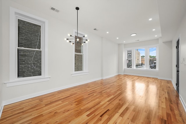 unfurnished living room with an inviting chandelier and light hardwood / wood-style floors