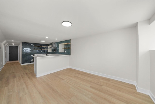 kitchen featuring kitchen peninsula, light hardwood / wood-style flooring, and wall chimney range hood