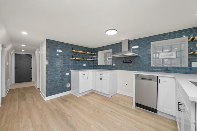 kitchen with white cabinetry, decorative backsplash, stainless steel dishwasher, wall chimney range hood, and light wood-type flooring