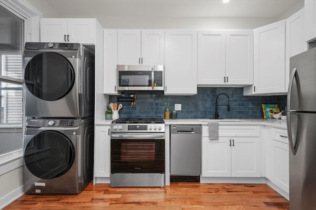 kitchen with stainless steel appliances, stacked washing maching and dryer, sink, and white cabinetry