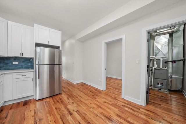 kitchen with white cabinetry, decorative backsplash, stainless steel fridge, and light wood-type flooring