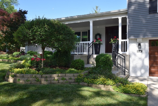 view of exterior entry with a yard, a garage, and a porch