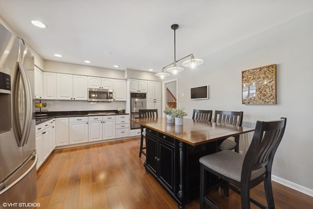 kitchen featuring pendant lighting, appliances with stainless steel finishes, white cabinetry, backsplash, and light hardwood / wood-style floors