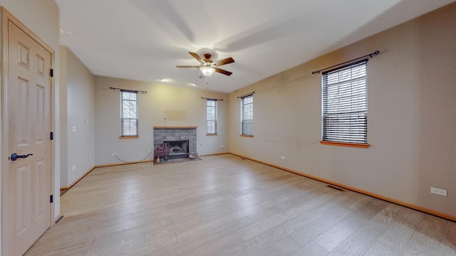 unfurnished living room with ceiling fan, a stone fireplace, and light wood-type flooring