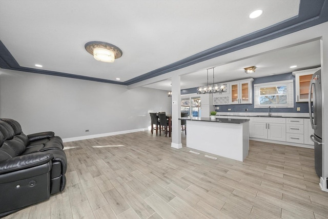 kitchen featuring pendant lighting, stainless steel refrigerator, white cabinetry, sink, and light hardwood / wood-style floors