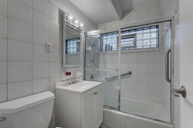 full bathroom with bath / shower combo with glass door, tile walls, vanity, and toilet