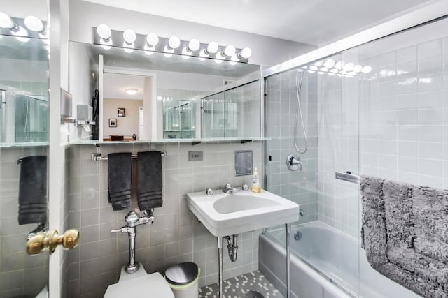 bathroom with bath / shower combo with glass door, tile walls, and toilet