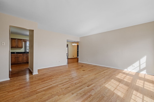 unfurnished room with light wood finished floors, a chandelier, and baseboards