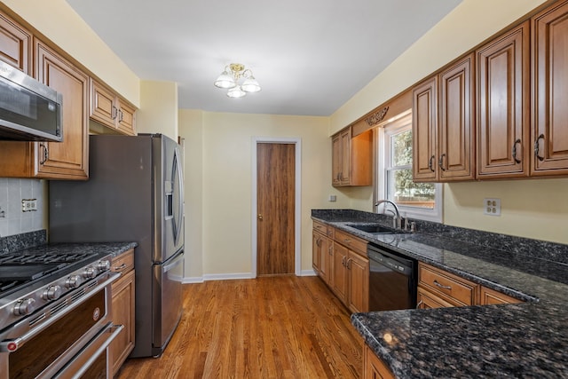 kitchen with tasteful backsplash, dark stone counters, light wood-style flooring, stainless steel appliances, and a sink