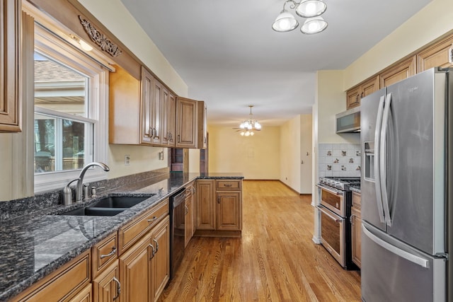 kitchen with light wood-style flooring, a sink, appliances with stainless steel finishes, brown cabinets, and a chandelier