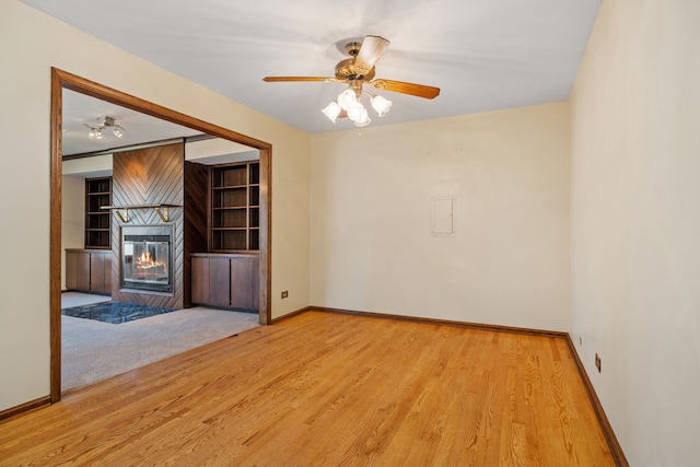 unfurnished living room featuring a glass covered fireplace, wood finished floors, baseboards, and a ceiling fan