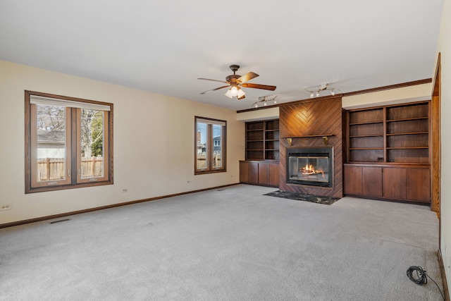 unfurnished living room with visible vents, baseboards, a fireplace with flush hearth, rail lighting, and light carpet