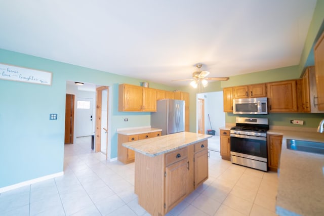 kitchen with sink, light tile patterned floors, ceiling fan, appliances with stainless steel finishes, and a kitchen island