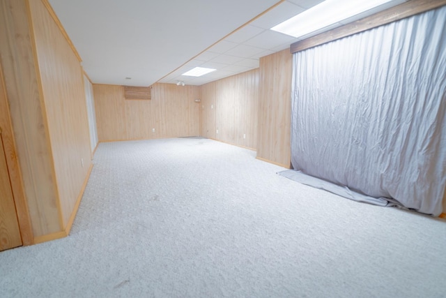 basement featuring light colored carpet, a drop ceiling, and wood walls