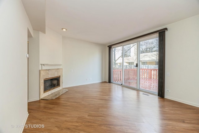 unfurnished living room with visible vents, a premium fireplace, baseboards, and wood finished floors