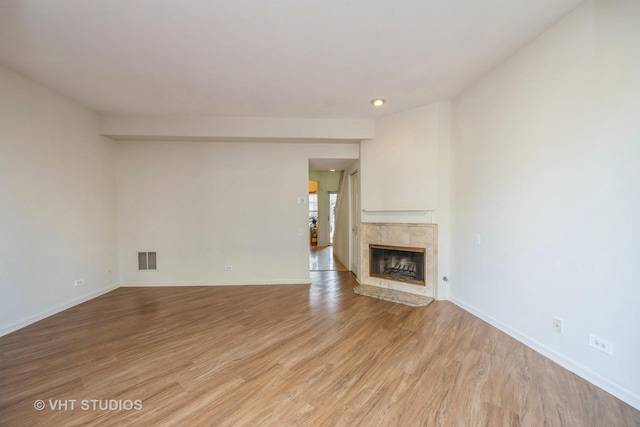 unfurnished living room with baseboards, a premium fireplace, visible vents, and light wood-style floors