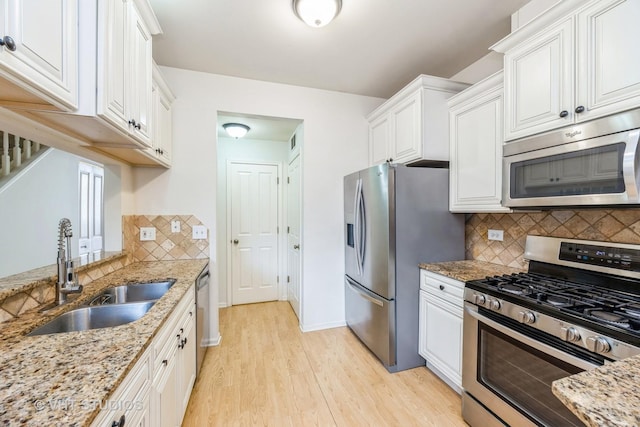 kitchen with light stone counters, stainless steel appliances, white cabinets, a sink, and light wood-type flooring