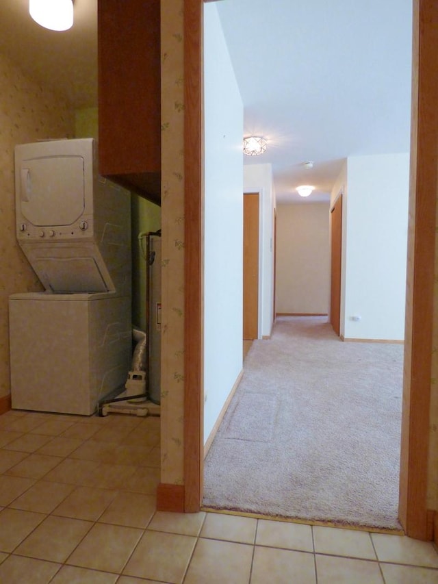 washroom featuring water heater, stacked washer and clothes dryer, and light tile patterned flooring