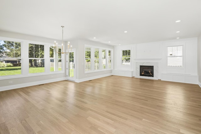 unfurnished living room with an inviting chandelier, a fireplace, and light hardwood / wood-style floors