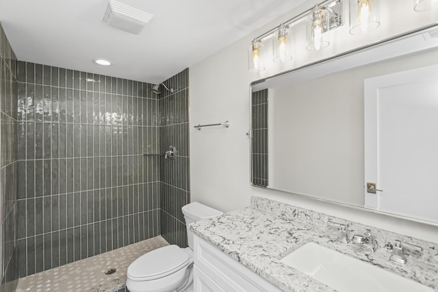 bathroom featuring a tile shower, vanity, and toilet