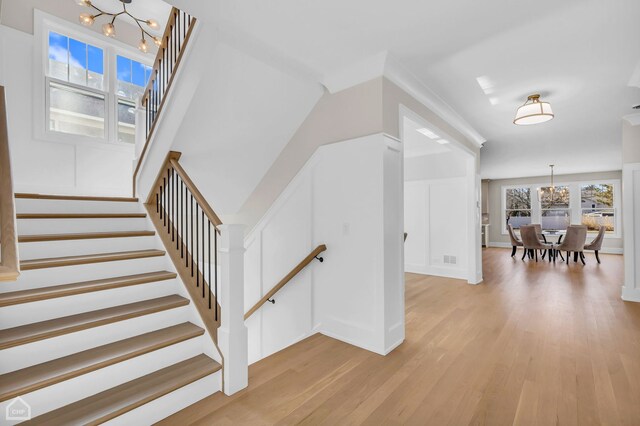 unfurnished living room featuring a healthy amount of sunlight, a premium fireplace, light hardwood / wood-style flooring, and a notable chandelier