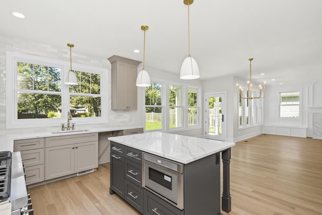 kitchen with sink, decorative light fixtures, light hardwood / wood-style flooring, a kitchen island, and decorative backsplash