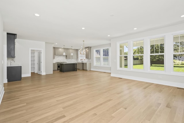 unfurnished living room with sink, light hardwood / wood-style floors, and a chandelier