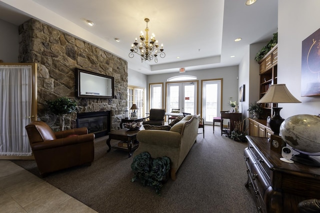 living room with french doors, dark colored carpet, a chandelier, a tray ceiling, and a fireplace