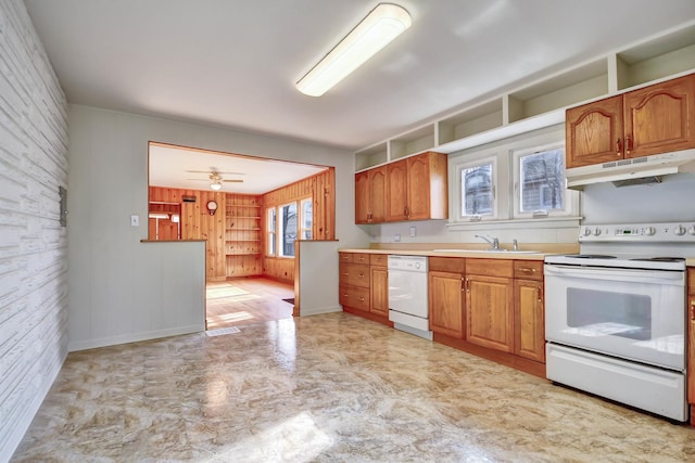 kitchen with ceiling fan, white appliances, sink, and wood walls