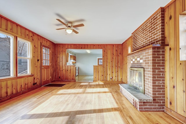 unfurnished living room featuring ceiling fan, light hardwood / wood-style floors, a brick fireplace, and wood walls