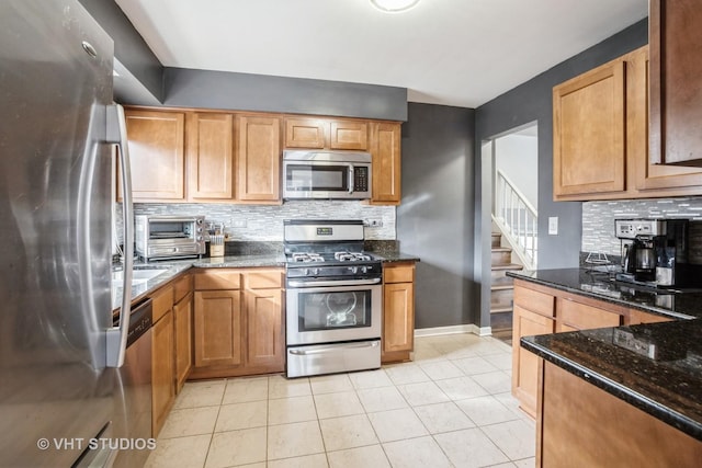 kitchen featuring dark stone countertops, light tile patterned floors, decorative backsplash, and appliances with stainless steel finishes