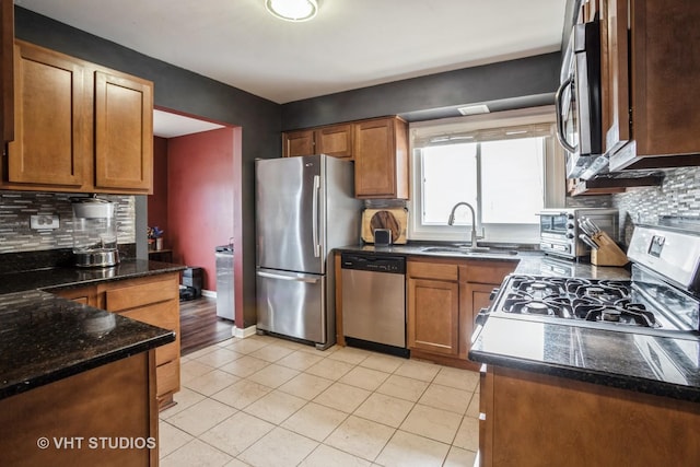 kitchen with sink, light tile patterned floors, appliances with stainless steel finishes, dark stone counters, and decorative backsplash