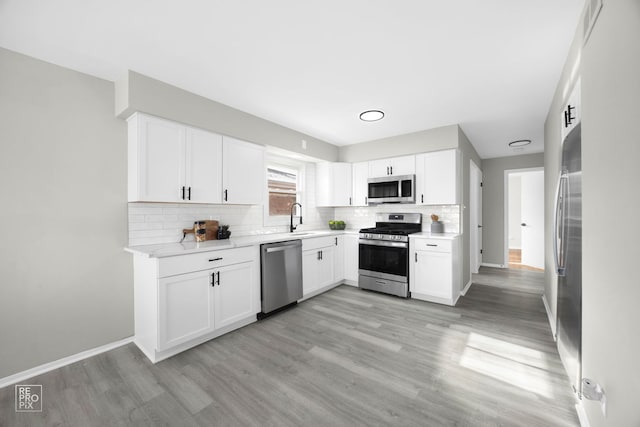 kitchen with stainless steel appliances, white cabinetry, sink, and light hardwood / wood-style floors