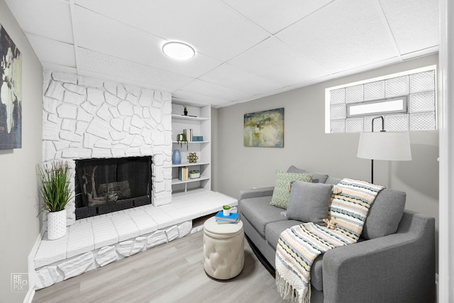 living room featuring wood-type flooring, a stone fireplace, a paneled ceiling, and built in features