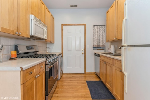 kitchen featuring appliances with stainless steel finishes, washer / clothes dryer, sink, decorative backsplash, and light wood-type flooring