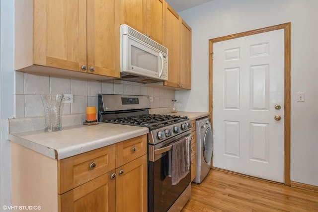 kitchen with stainless steel range with gas stovetop, washer / dryer, light wood-type flooring, and backsplash