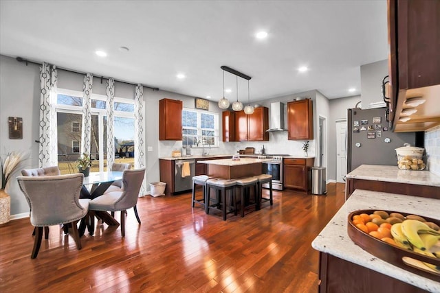 kitchen featuring appliances with stainless steel finishes, a kitchen island, decorative light fixtures, tasteful backsplash, and wall chimney range hood