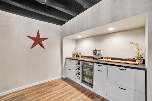 bar featuring white cabinetry, light hardwood / wood-style floors, beverage cooler, and beamed ceiling