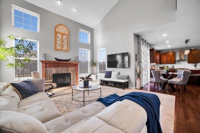 living room with a wealth of natural light, wood-type flooring, a tile fireplace, and a high ceiling