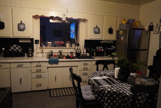 kitchen featuring dark tile patterned floors, sink, white cabinets, and stainless steel refrigerator