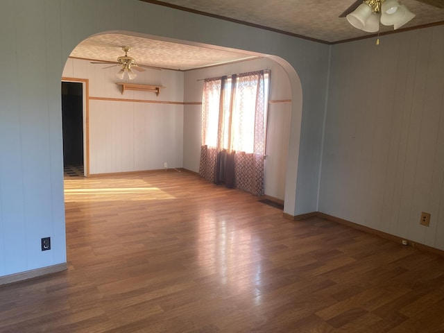 spare room with dark wood-type flooring, ornamental molding, ceiling fan, and wood walls