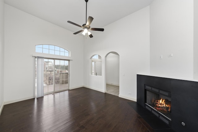 unfurnished living room with ceiling fan, dark hardwood / wood-style floors, and a towering ceiling