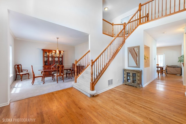 stairway with hardwood / wood-style flooring, ornamental molding, and a notable chandelier