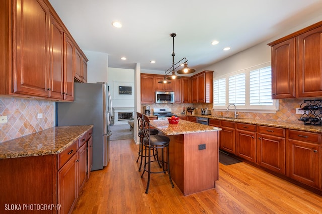 kitchen with stainless steel appliances, light hardwood / wood-style floors, hanging light fixtures, and a kitchen island