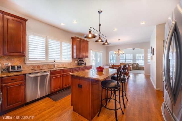 kitchen featuring a center island, hanging light fixtures, appliances with stainless steel finishes, hardwood / wood-style floors, and decorative backsplash