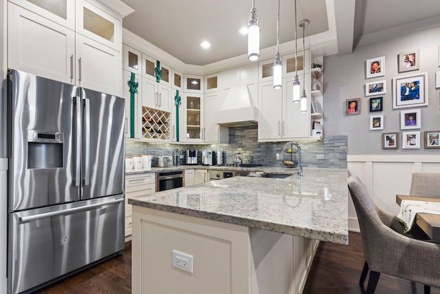 kitchen featuring sink, custom exhaust hood, white cabinetry, appliances with stainless steel finishes, and pendant lighting